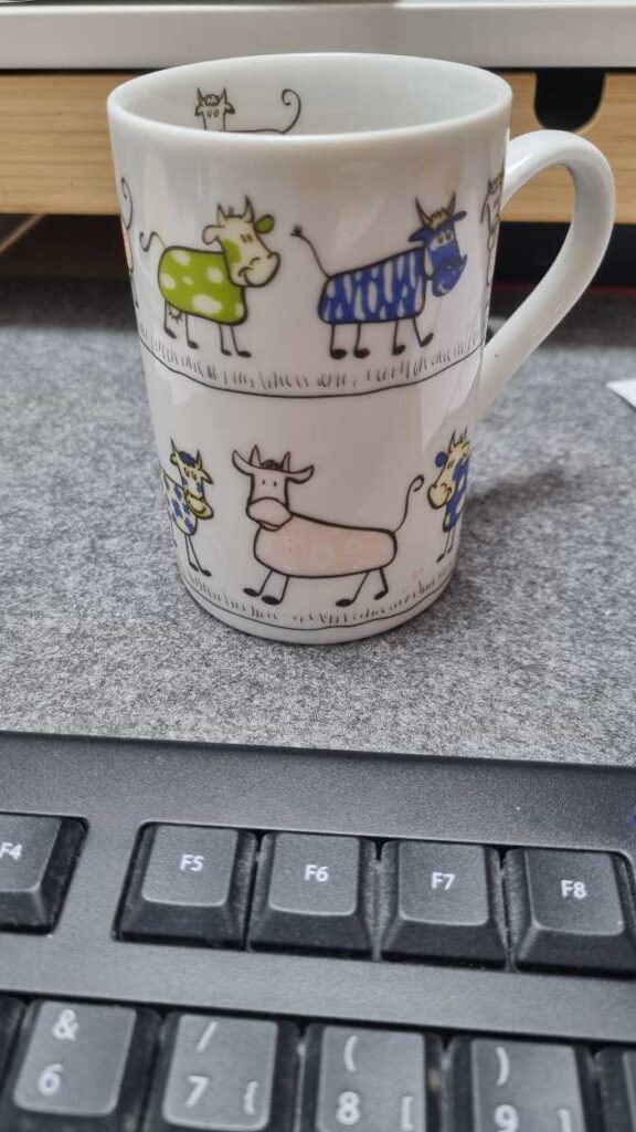 Schreibtisch mit Kaffebecher auf dem Kühe zu sehen sind.