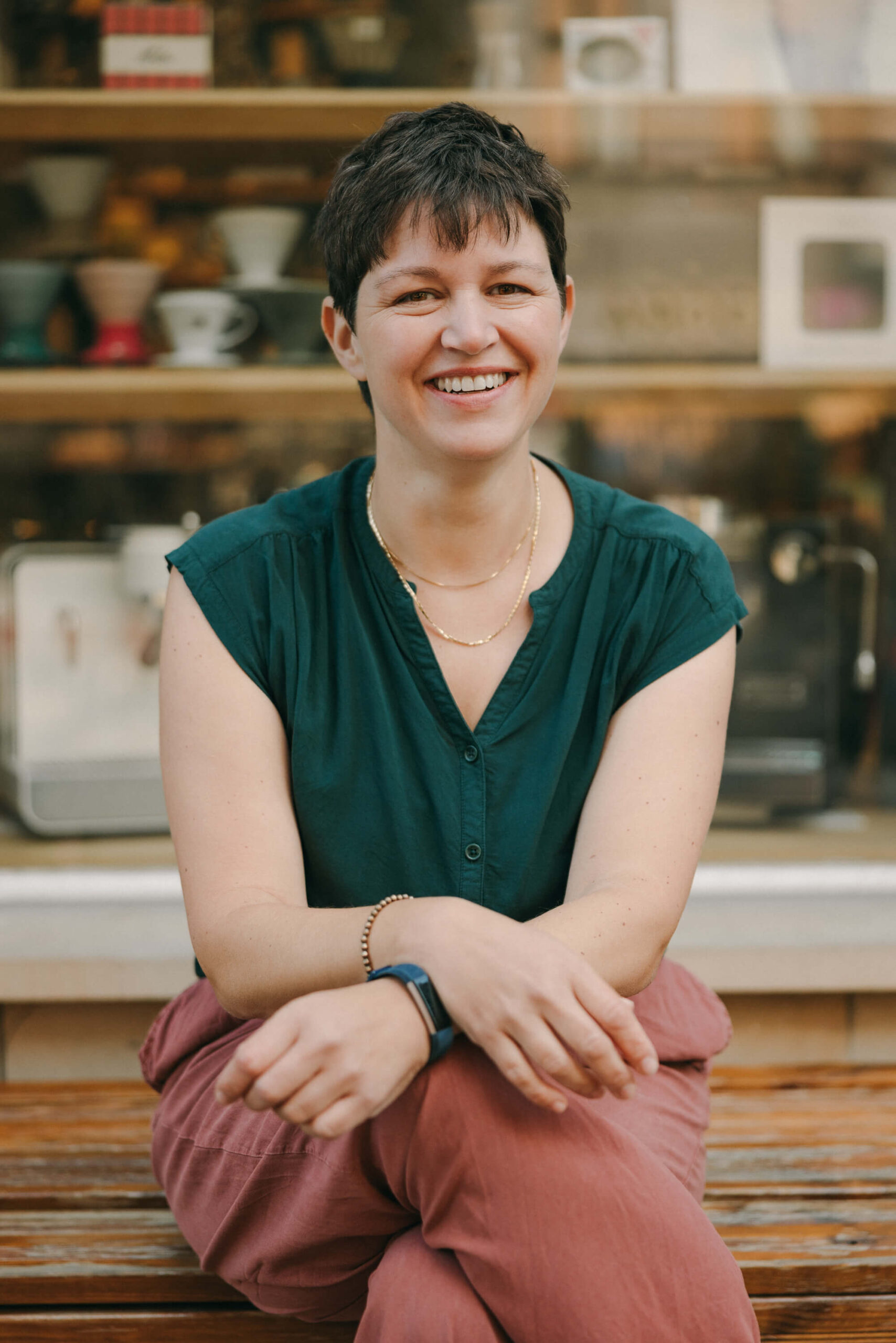 Katja Andergassen, Expertin für herausforderndes Verhalten in Kitas, sitzt lächelnd auf einer Bank vor einem Café. Sie begleitet pädagogische Fachkräfte in Weiterbildungen und Prozessbegleitungen, um Kinder mit herausforderndem Verhalten besser zu verstehen und sicher zu begleiten.